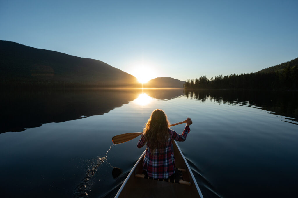 Woman paddling a canoe on a calm lake at sunrise, symbolizing the journey of individual therapy and personal growth with a compassionate guide